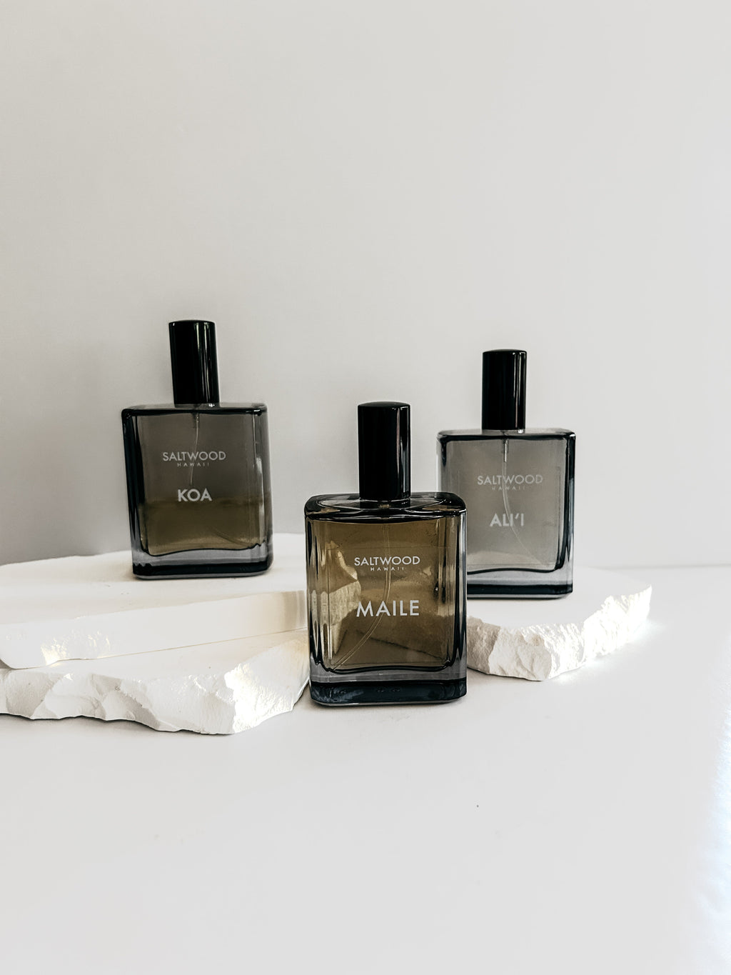 Three black perfume bottles labeled 'KOA', 'MAILE', and 'ALI' on a white surface with a light gray background.